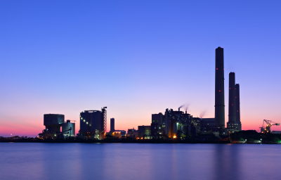 A silhouette of an industrial facility at dusk, featuring smokestacks and various structures beside a body of water, representing sectors like oil recovery and water treatment relevant to Vista Projects' engineering consulting services.