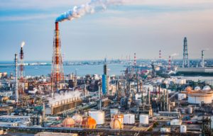 Aerial view of an industrial facility with tall smokestacks and various structures, showcasing a complex of refineries and storage tanks, representing the oil and petrochemical industries.