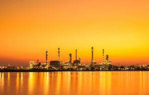 Industrial facility at sunset, featuring multiple structures such as smokestacks and towers, reflecting on water. This image represents the types of projects that Vista Projects, an engineering consulting firm, works on in sectors like petrochemicals and oil recovery.