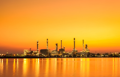 Industrial facility at sunset, featuring multiple structures such as smokestacks and towers, reflecting on water. This image represents the types of projects that Vista Projects, an engineering consulting firm, works on in sectors like petrochemicals and oil recovery.