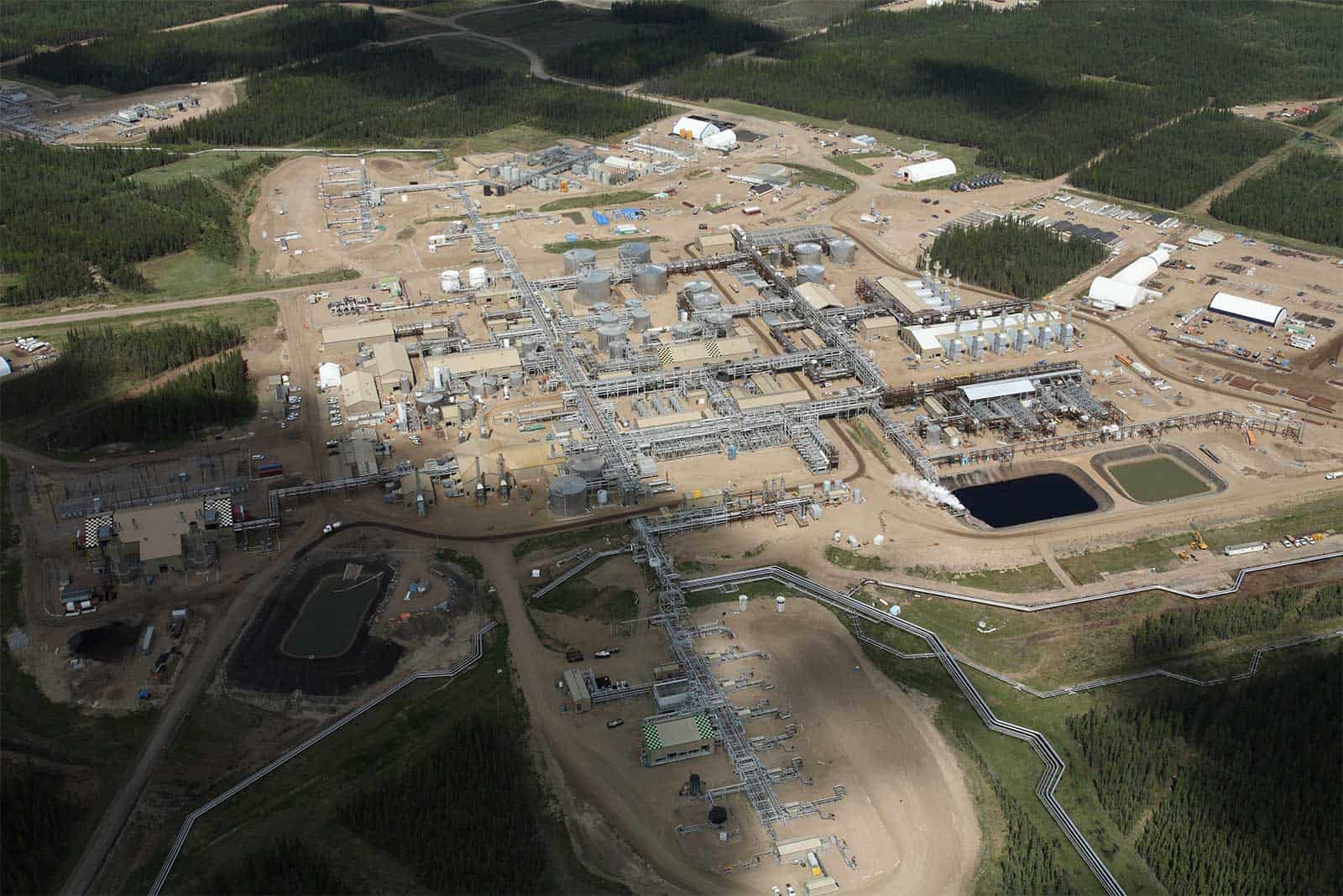 Aerial view of an industrial facility featuring multiple buildings, storage tanks, pipelines, and equipment, set in a forested area. The site shows clear organization of operational areas, highlighting engineering and technology infrastructure for industrial processes.