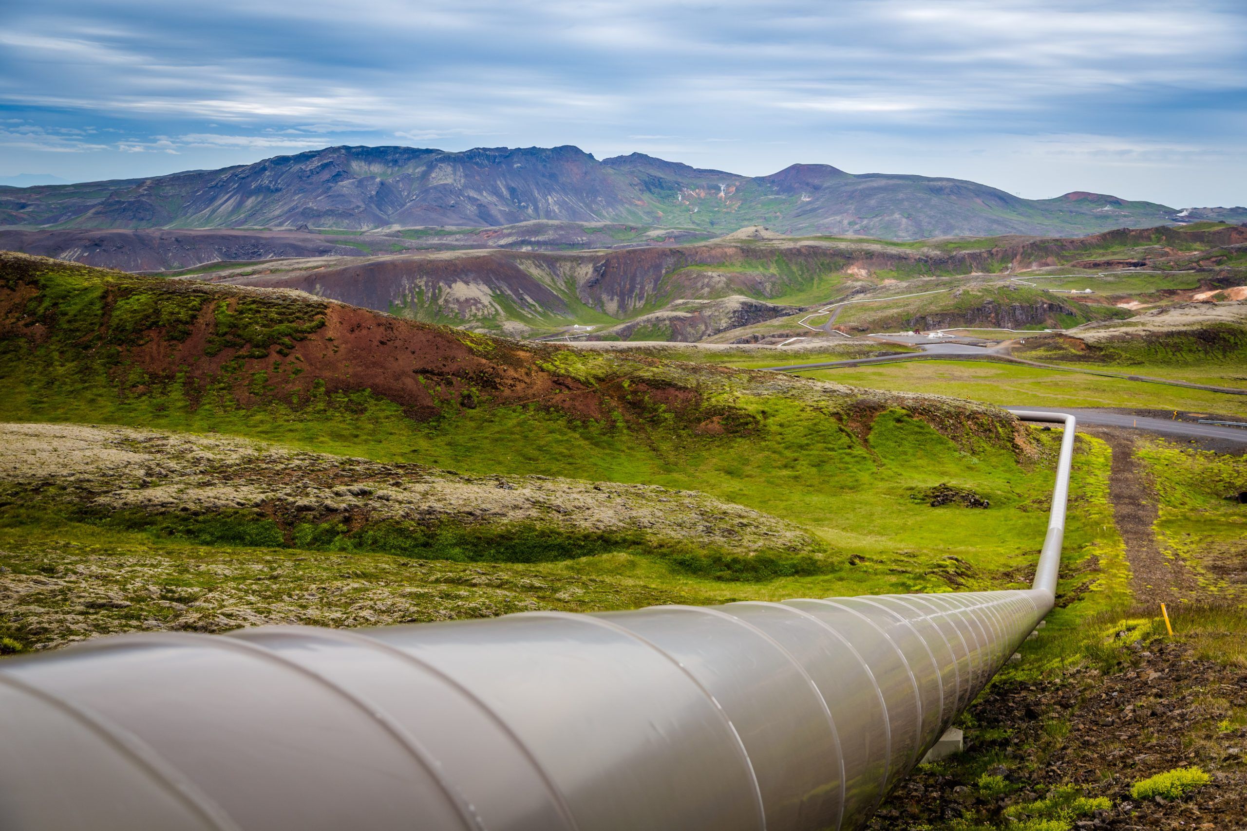 A pipeline runs through a green and rocky landscape, surrounded by rolling hills and mountains. The scene illustrates the integration of infrastructure in natural settings, highlighting the importance of quality engineering in pipeline management.