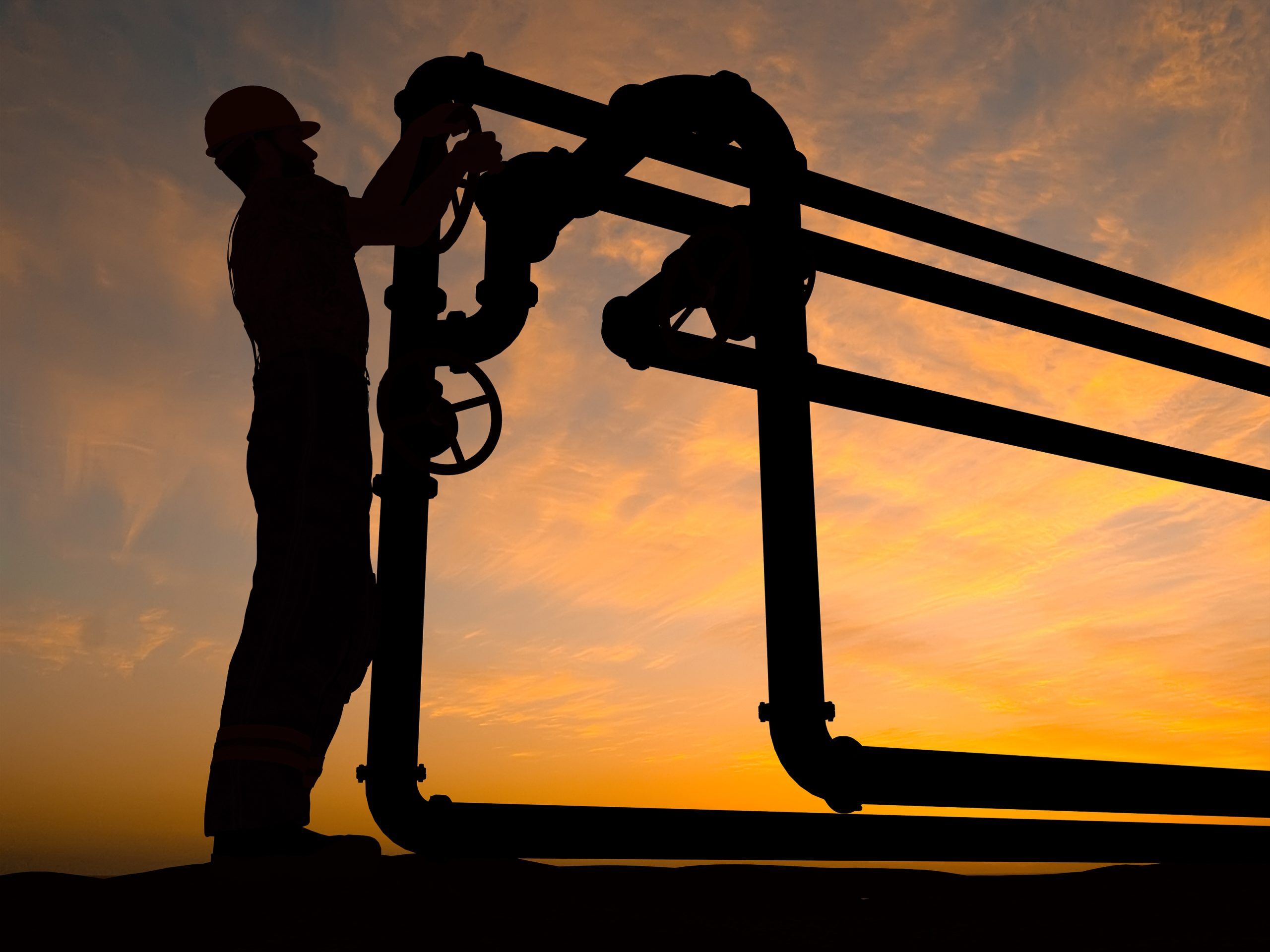 A worker adjusts industrial piping equipment during sunset, highlighting safety measures in the energy industry. This image emphasizes the importance of safety protocols and proper maintenance in high-risk environments.