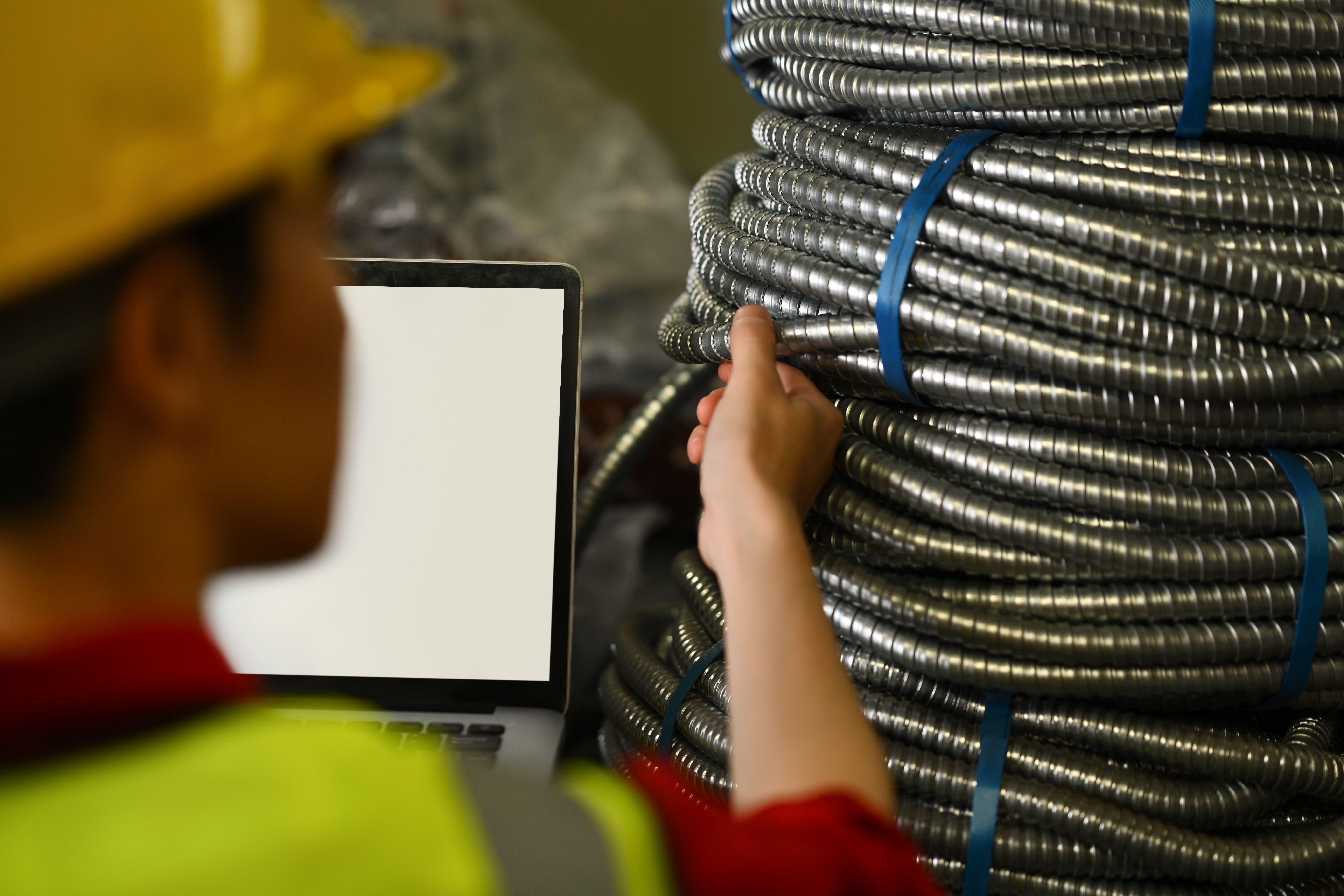 worker in safety gear inspecting coiled metal conduit