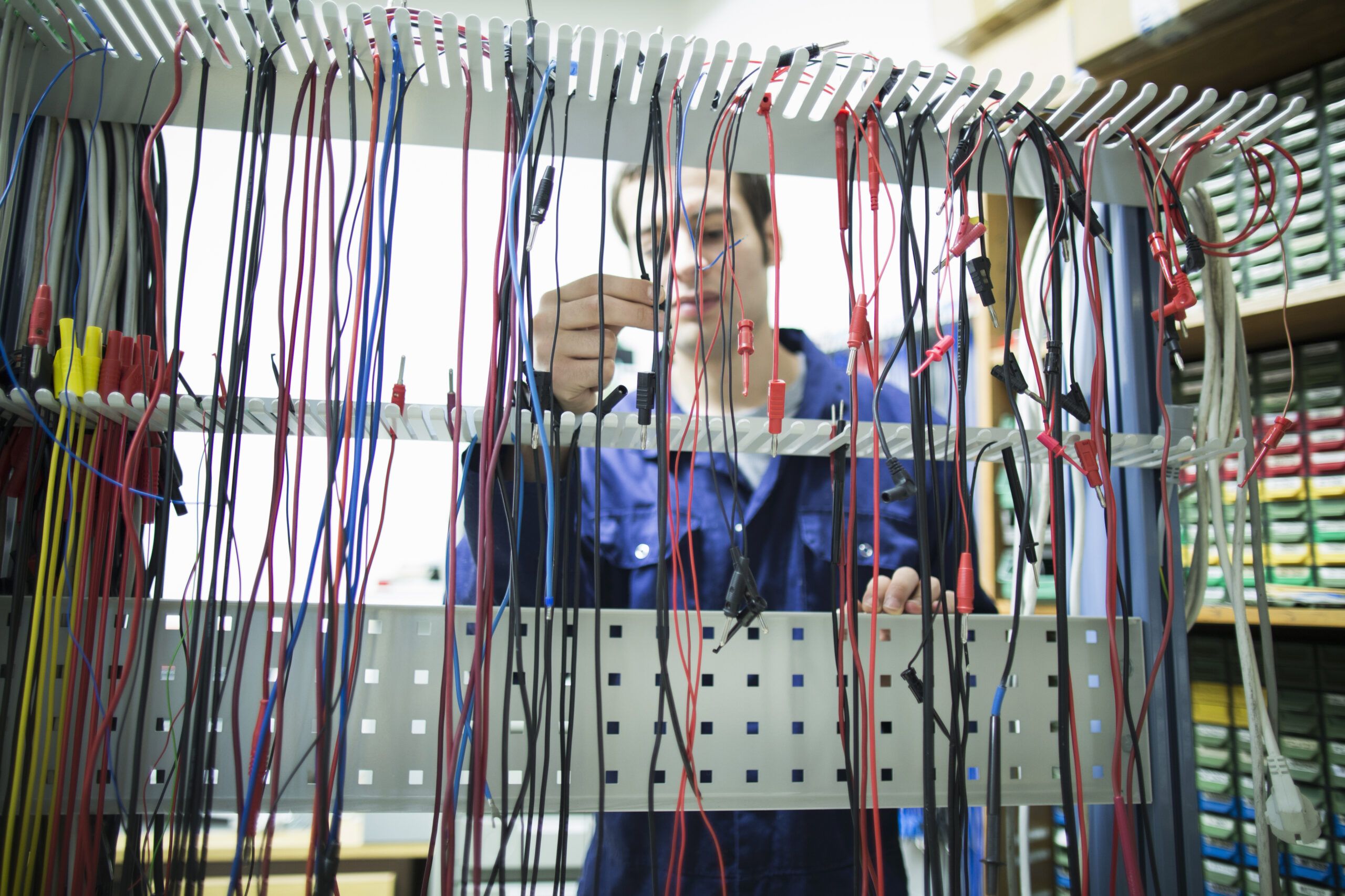 Electrician organizing a variety of industrial cables on a vertical rack in a workshop.