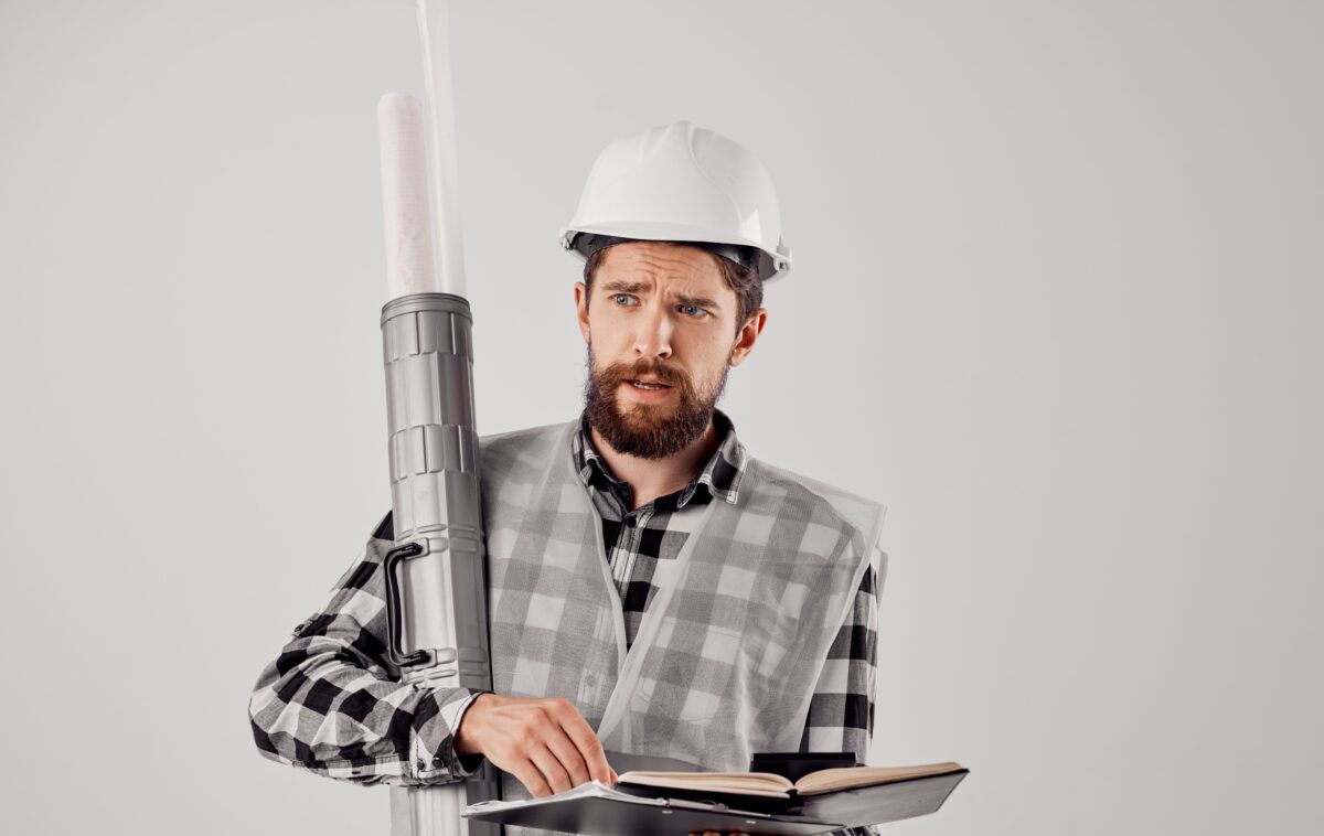 Concerned civil engineer holding blueprints and notebook, managing complex project challenges.