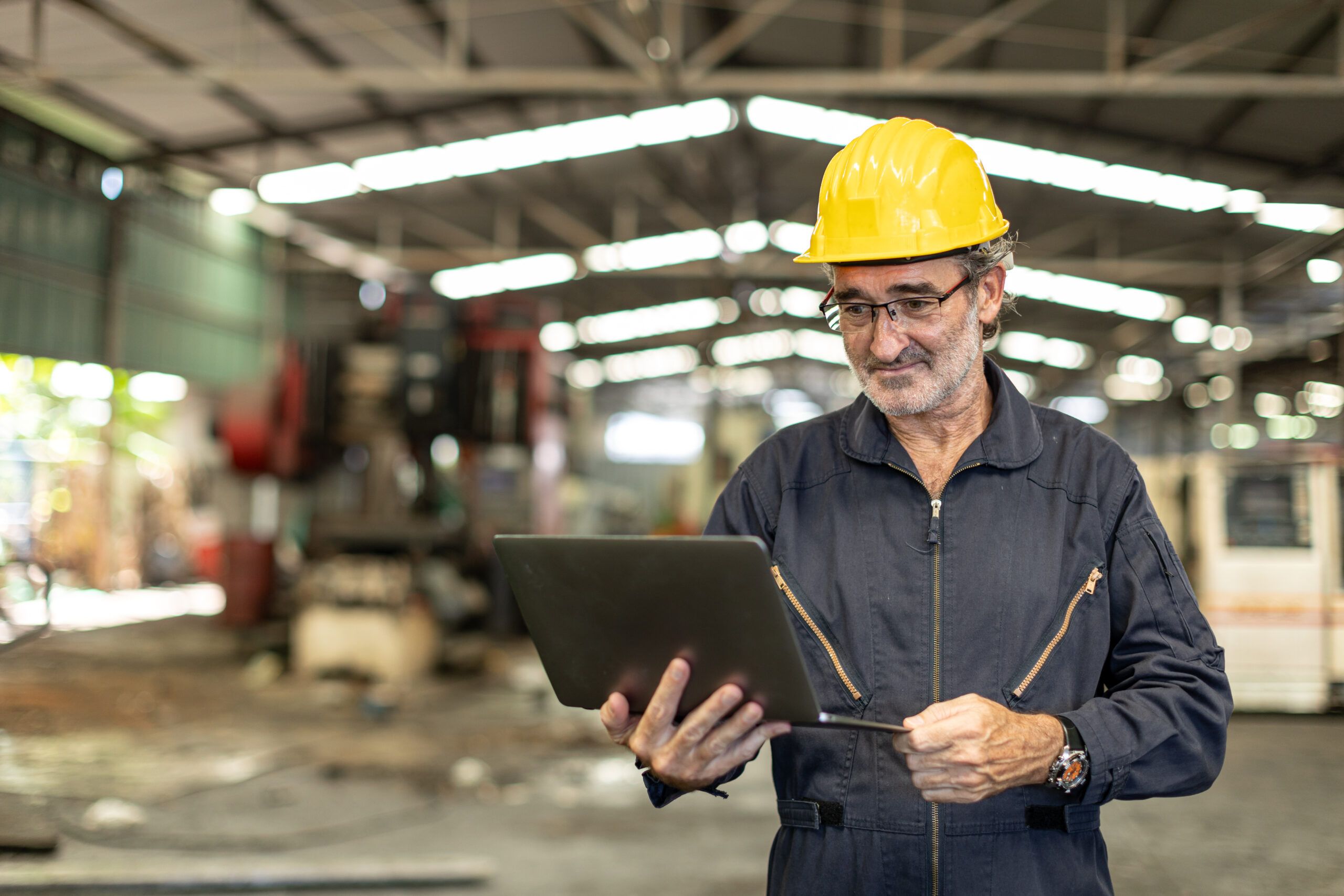 Senior electrical engineer using a laptop in an industrial facility for project planning and portfolio documentation.