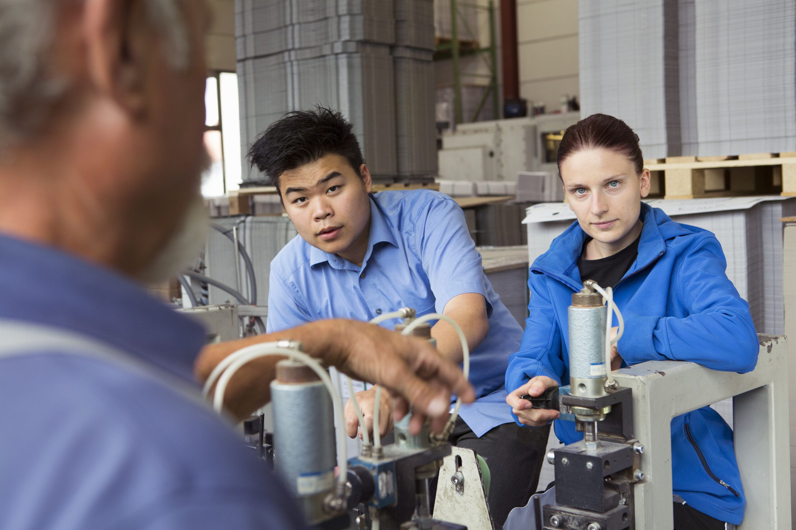 Mechanical engineering mentor explaining industrial machinery to young engineers in a factory setting