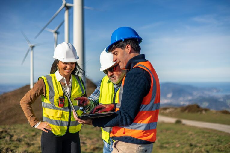 Civil engineers reviewing wind farm site data on a laptop near wind turbines during an energy infrastructure inspection